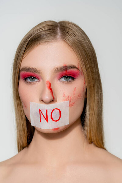 Woman with blood on face and card with lettering no on lips isolated on grey 
