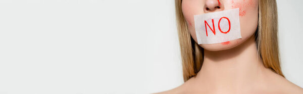 Cropped view of young woman with blood on face and card with lettering no on lips isolated on grey, banner 