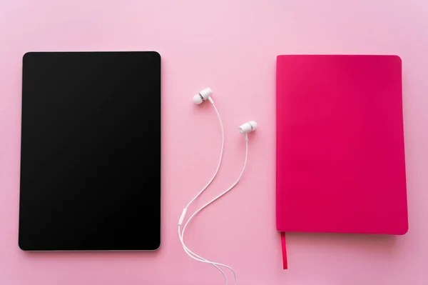 イヤフォンの近くに空白の画面とピンクの明るいノートブックを持つデジタルタブレットのトップビュー — ストック写真