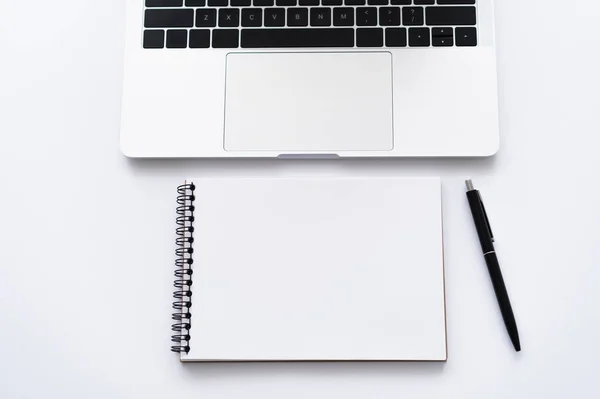 白色笔记本电脑旁边的笔记本电脑和钢笔的顶部视图 — 图库照片