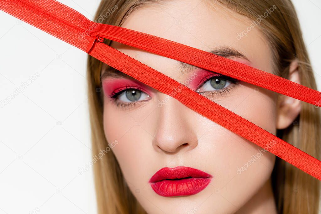 Young woman with red lips looking at camera near zipper isolated on white 