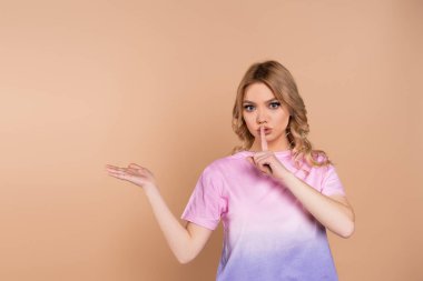 Güzel bir kadın sus işareti gösteriyor ve bej üzerinde elle izole edilmiş işaret ediyor.