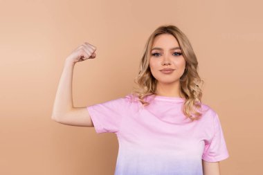 positive woman demonstrating power while looking at camera isolated on beige