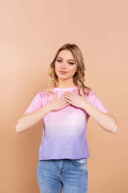grateful woman with wavy hair holding hands on chest isolated on beige