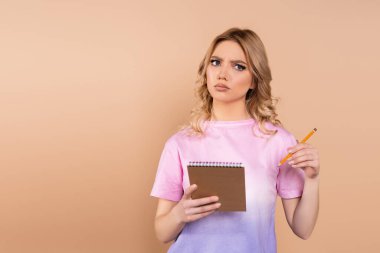 pensive woman with pencil and notepad looking away isolated on beige