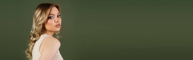 pretty woman with wavy hair looking at camera isolated on green, banner