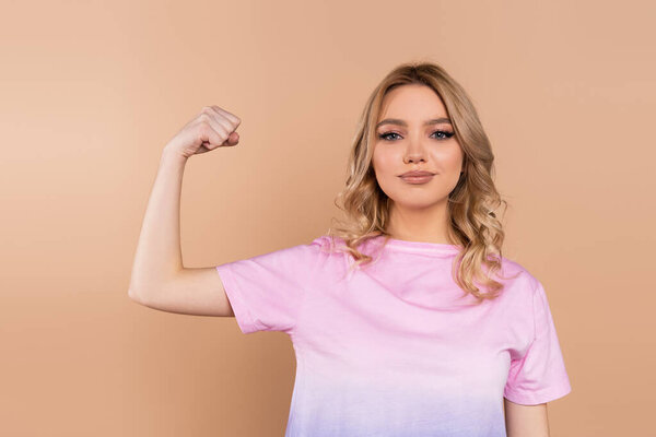 positive woman demonstrating power while looking at camera isolated on beige