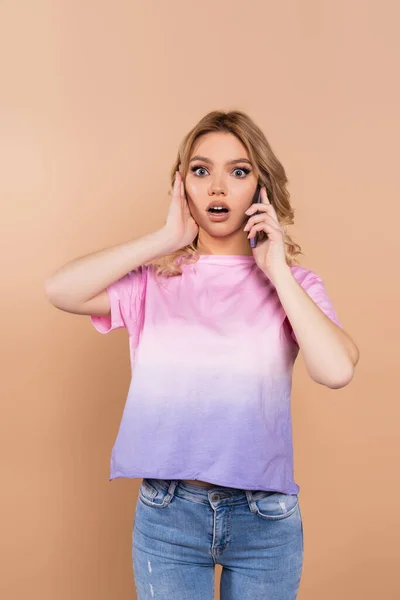 Mujer Emocionada Tocando Cara Mientras Habla Teléfono Inteligente Aislado Beige — Foto de Stock