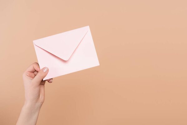 partial view of female hand with postal envelope isolated on beige