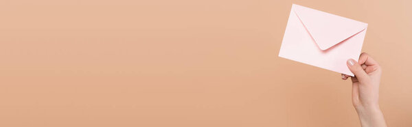 cropped view of woman holding envelope isolated on beige, banner