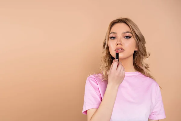 Young Woman Looking Camera While Applying Lipstick Isolated Beige — Foto Stock