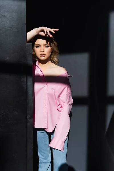 Соблазнительная Женщина Розовой Рубашке Смотрит Камеру Освещении Возле Черной Стены — стоковое фото