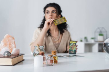 Candle and witchcraft supplies near blurred gypsy fortune teller with tarot cards at home 