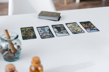 KYIV, UKRAINE - FEBRUARY 23, 2022: Tarot cards near blurred witchcraft supplies on table 