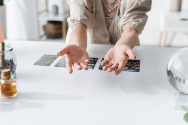 Masadaki tarot kartlarının yanında uzanan orta boy ellerin kırpılmış görünümü 