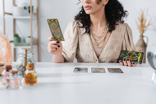 KYIV, UKRAINE - FEBRUARY 23, 2022: Cropped view of fortune teller holding tarot cards near crystal at home 