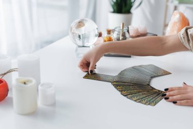 KYIV, UKRAINE - FEBRUARY 23, 2022: Cropped view of fortune teller holding tarot near blurred candles on table 