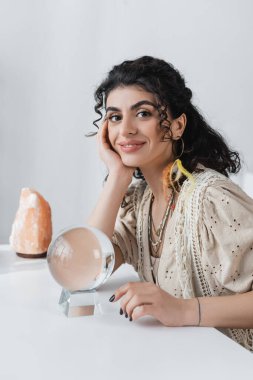 Gülümseyen çingene falcı masanın yanındaki küreye ve kristale bakıyor. 