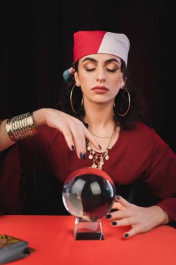 Gypsy fortune teller with closed eyes touching magic orb isolated on black 