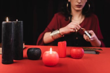 Cropped view of blurred fortune teller holding matches near candles and tarot cards isolated on black 
