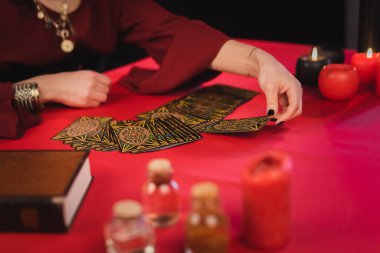 KYIV, UKRAINE - FEBRUARY 23, 2022: Cropped view of medium taking tarot card near blurred jars and book on table 