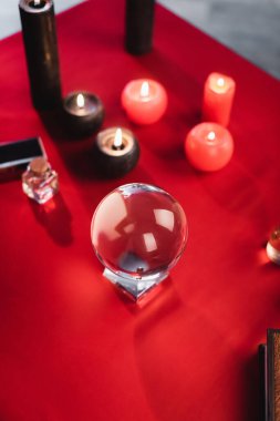 Top view of glass orb near blurred candles and book on table  clipart