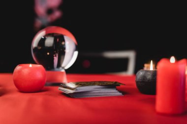 Tarot cards near burning candles and blurred orb on black 