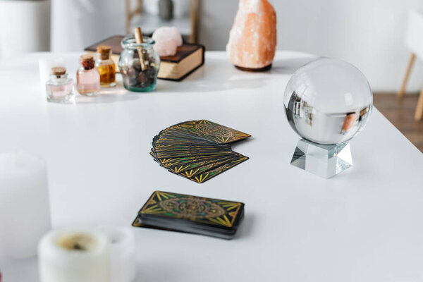 KYIV, UKRAINE - FEBRUARY 23, 2022: Tarot cards and magic orb near blurred candles on table 