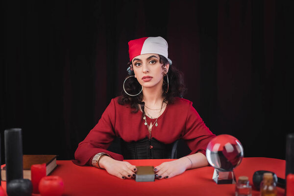 Gypsy fortune teller looking at camera near tarot cards isolated on black 