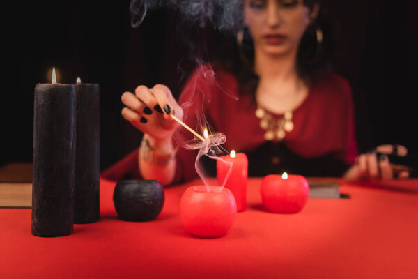 Cropped view of medium holding match while burning candles on table isolated on black 