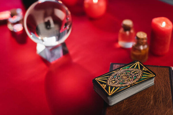 KYIV, UKRAINE - FEBRUARY 23, 2022: Close up view of tarot cards on book near blurred orb and candles on table 