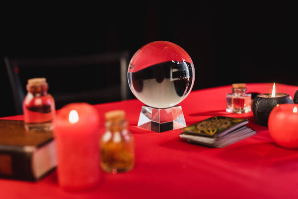 Magic orb near tarot cards and candles on table isolated on black 