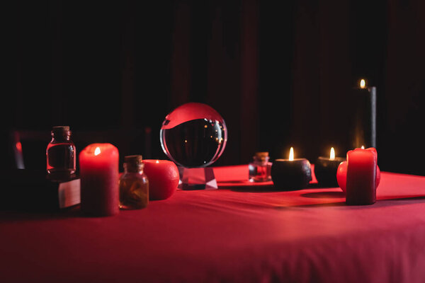 Magic orb near burning candles on table isolated on black 