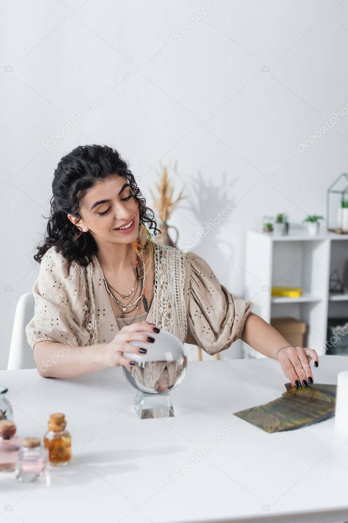 Smiling gypsy medium touching magic orb and tarot cards on table 
