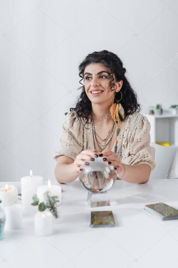 Cheerful gypsy medium touching orb near candles and tarot on table 