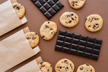 Top view of chocolate bars and cookies in craft packages on brown background 