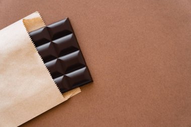Top view of dark chocolate bar in craft package on brown background 
