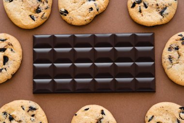 Top view of chocolate bar in frame from cookies on brown background 