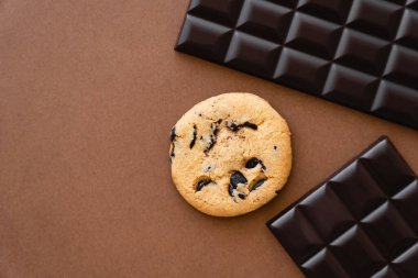 Top view of cookie near dark chocolate bars on brown background 