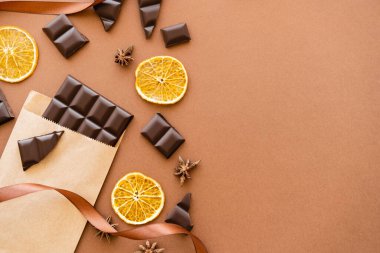 Top view of chocolate in craft package, orange slices and anise on brown background 