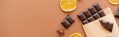 Top view of anise, dry orange slice and chocolate in craft package on brown background, banner 