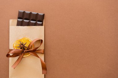 Top view of chocolate in craft package with orange slice and anise on brown background 