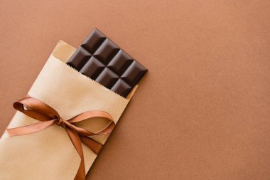 Top view of dark chocolate bar in craft package with ribbon on brown background 