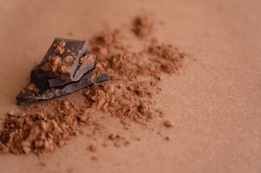 Kahverengi arkaplanda koyu çikolata ve kakao tozunun fotokopi alanı ile yakın görüntüsü