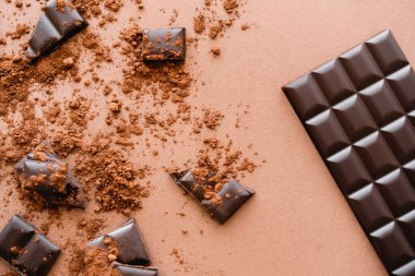 Top view of chocolate bar near pieces and dry cocoa on brown background 