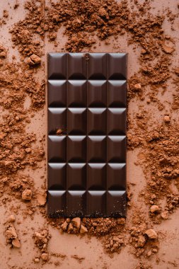 Top view of dark chocolate bar and cocoa on brown background 