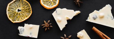 Top view of dry orange slices, spices and white chocolate on black background, banner 