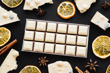 Top view of milk chocolate near natural spices and dry orange slices on black background