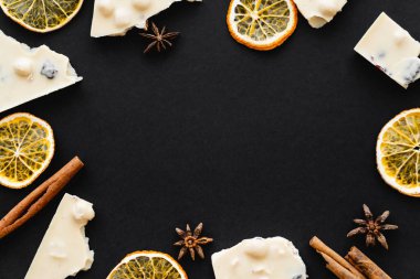 Top view of frame from white chocolate, dry orange slices and spices on black background