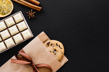 Top view of cookie in craft package, chocolate and dry spices on black surface 